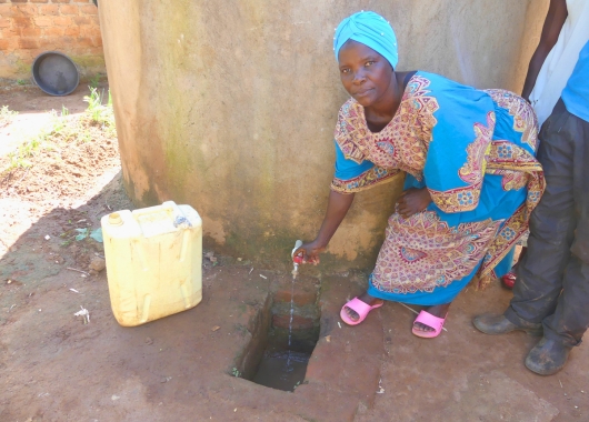 Eine Frau dreht neben einem Kanister den Wasserhahn an einer Säule auf