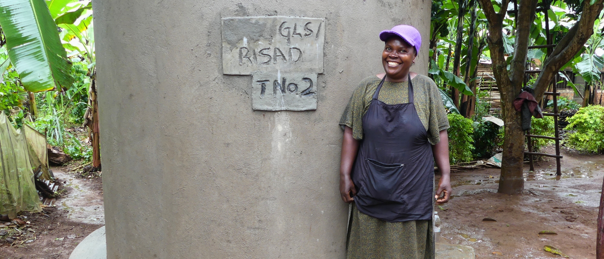 Eine lächelnde Frau steht vor einem runden Betonbau, im Hintergrund Pflanzen und eine Leiter