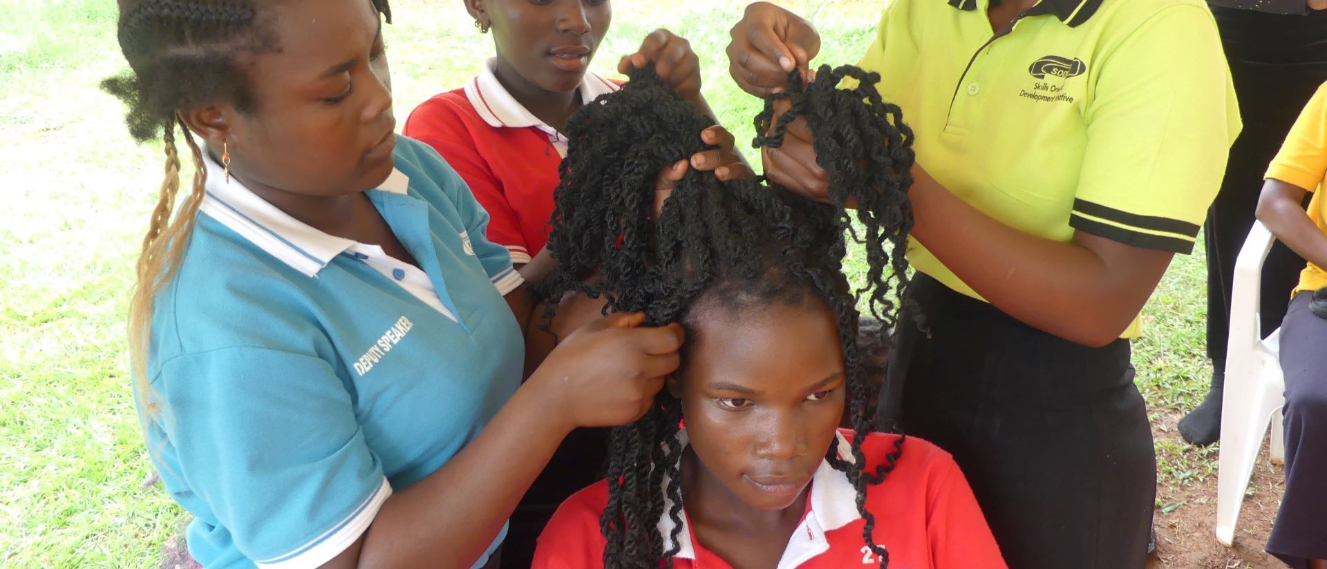 Eine junge Frau im Zentrum des Bildes wird von drei anderen jungen Frauen frisiert.