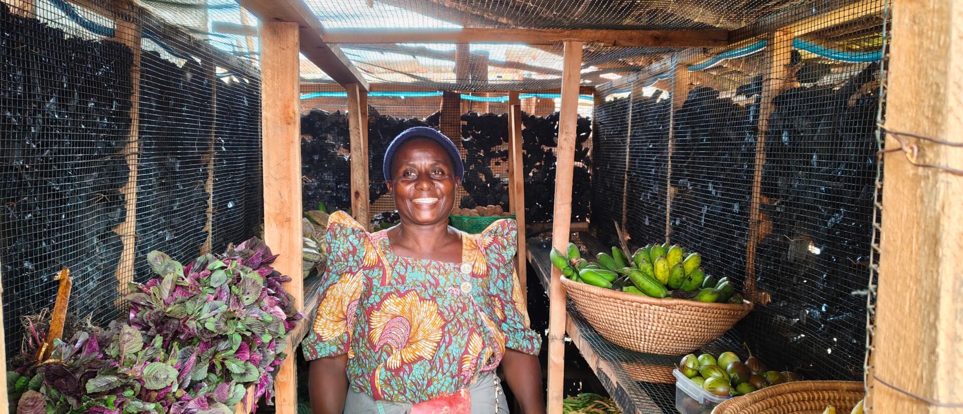 Eine Frau steht in einem Raum aus mit Kohle gefüllten Mauergestellen zwischen Bananen und Blattgemüse.