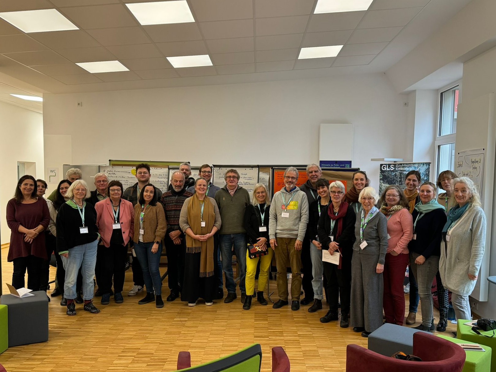 26 Personen stehen für ein Gruppenbild zusammen und lächeln in die Kamera.