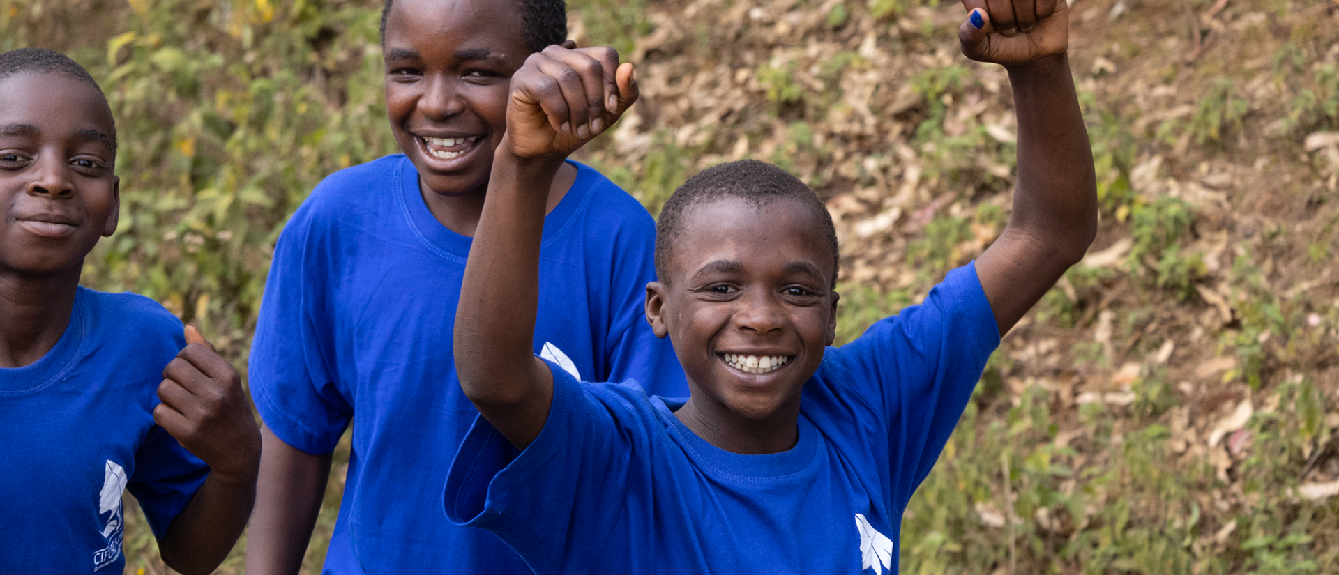 Ein Junge mit blauen T-Shirt wirft beide Arme in die Luft.