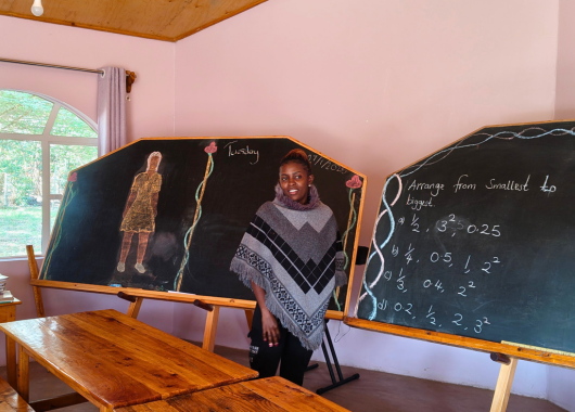 Eine junge Frau steht vor zwei Tafeln. Auf der rechten Tafel wurde gerechnet, auf der linken wurde eine Frau gezeichnet.