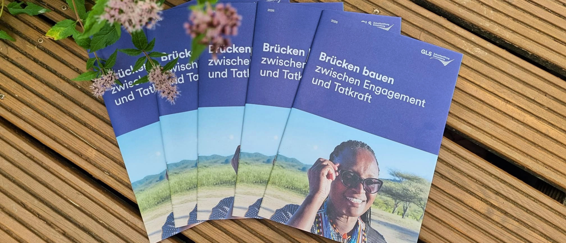 Ein Stapel Broschüren mit dem Titel "Brücken bauen zwischen Engagement und Tatkraft" liegt auf Holzbohlen.