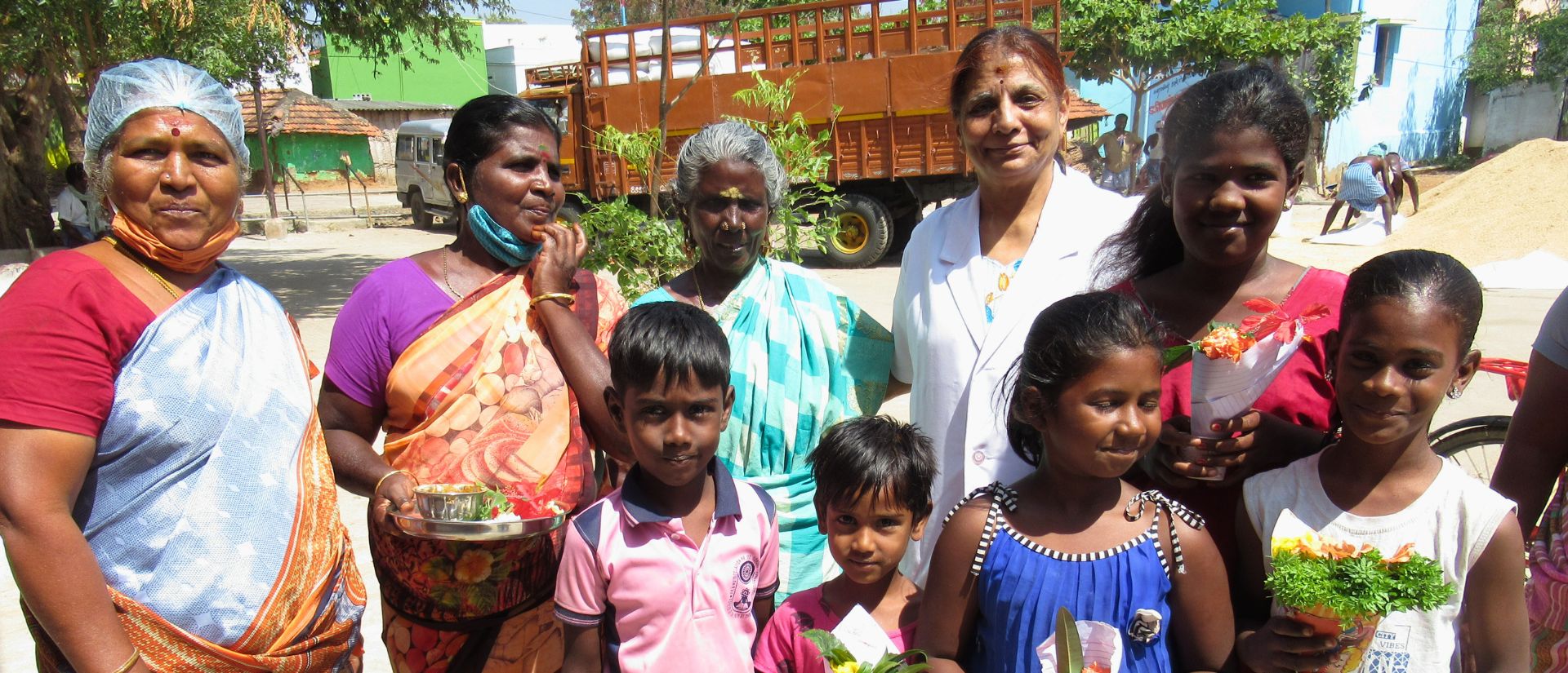Eine Reihe bunt gekleideter Frauen steht hinter einer Reihe von Kindern auf einem Platz