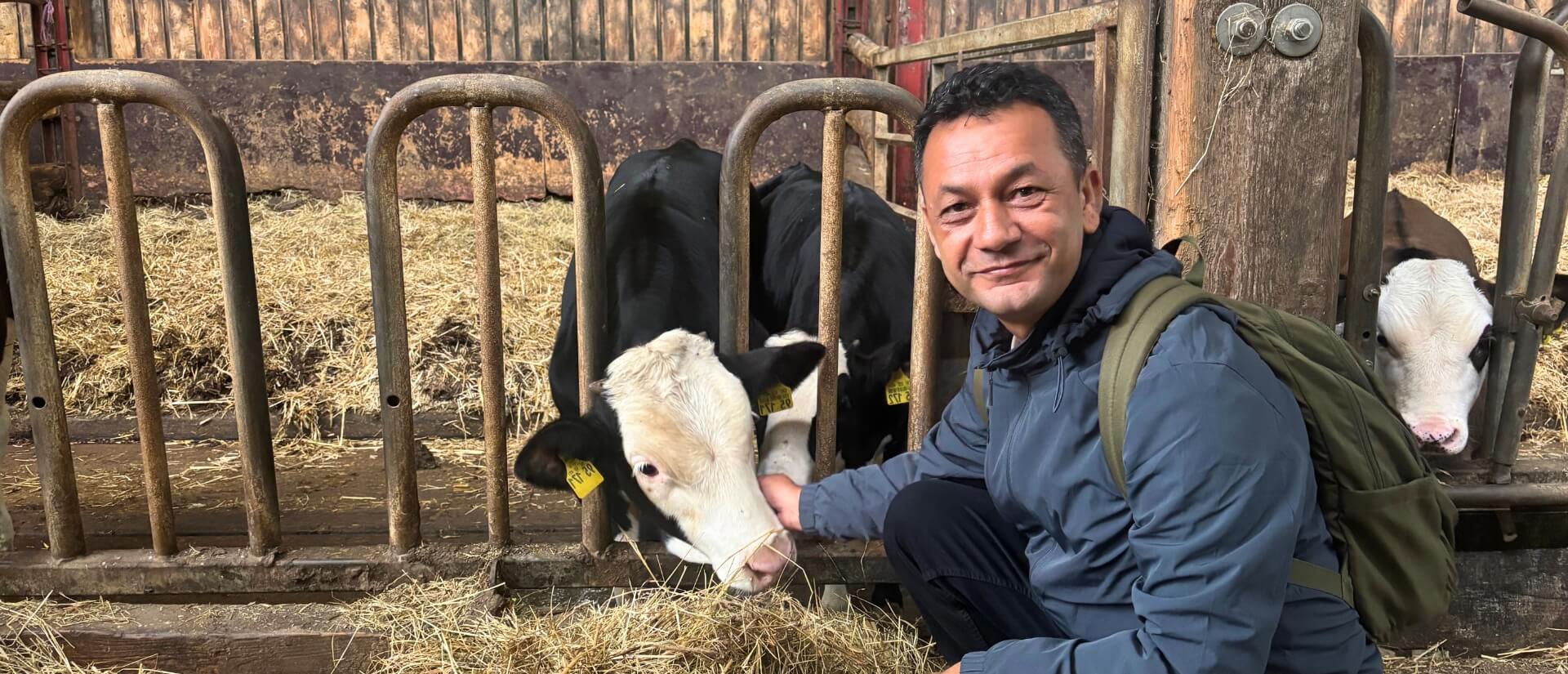 Ein Mann schaut in die Kamera, während er vor zwei Kälbchen hockt und sie streichelt