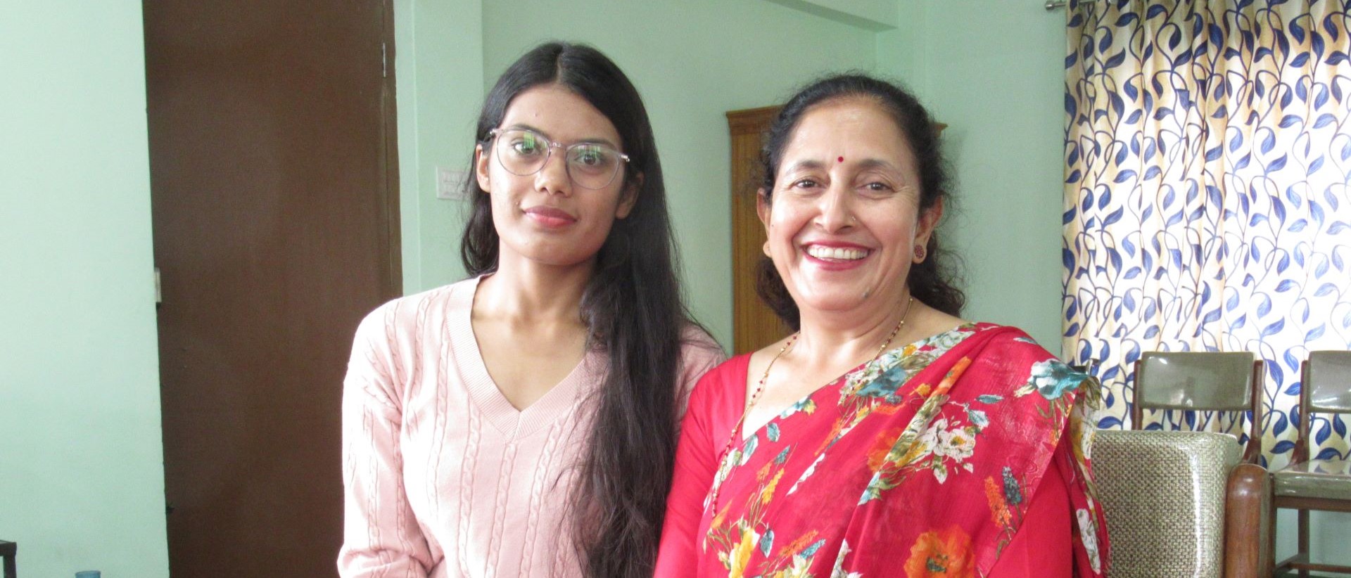 Zwei Frauen sitzen nebeneinander und lächeln in die Kamera. 