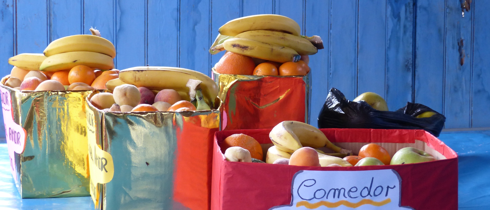 Golden und rot beklebte Kartons gefüllt mit Obst vor blauem Hintergrund
