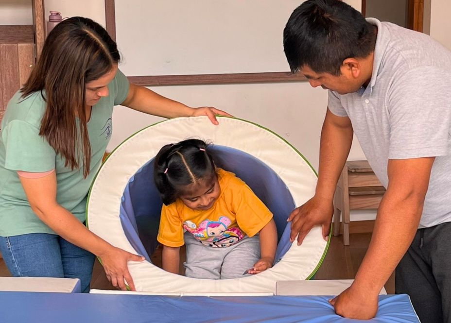 Ein Mann und eine Frau halten einen gepolsterten Trichter, in dem ein kleines Mädchen sitzt.