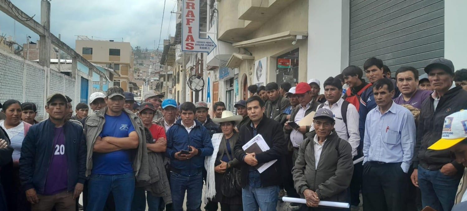 Eine Gruppe von Menschen stehen auf einer Straße in Peru zusammen für ein Gruppenfoto. Ernst schauen sie in die Kamera.