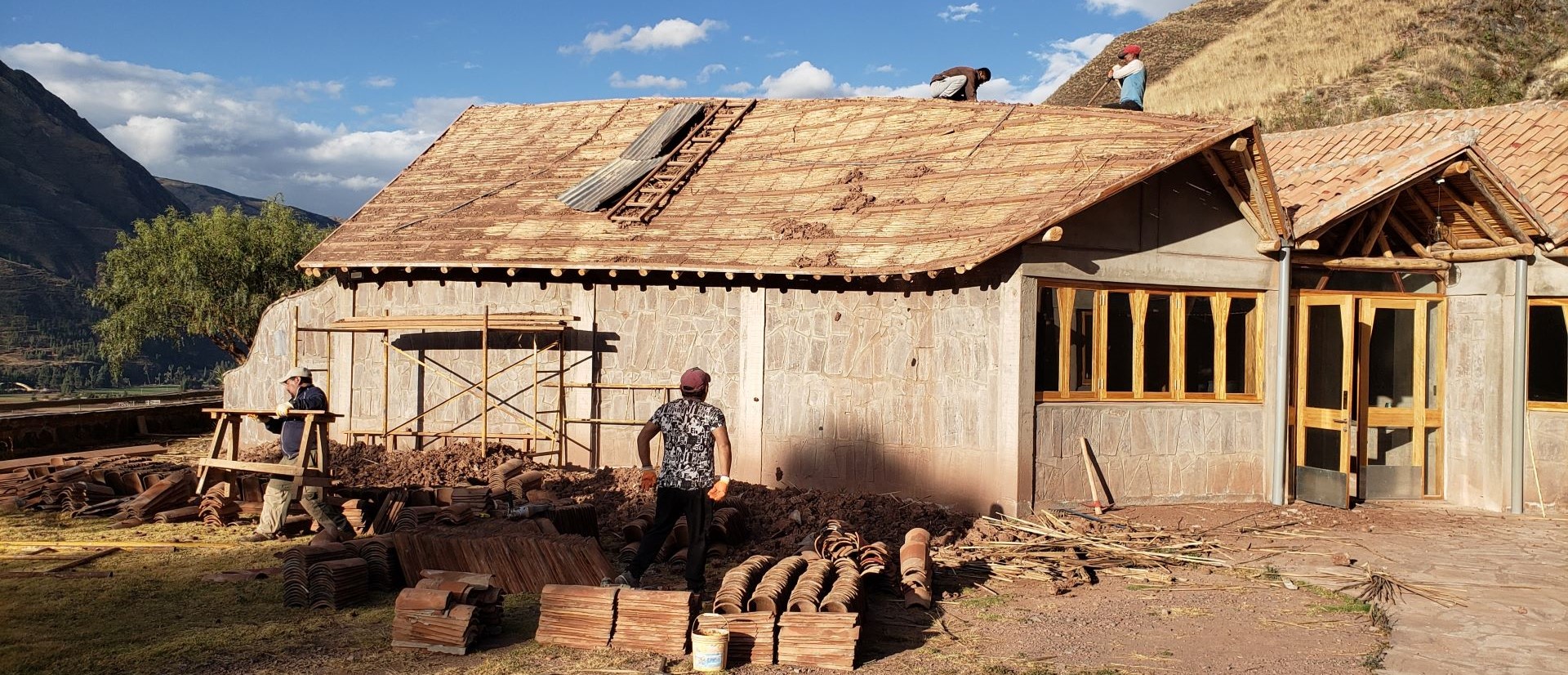 Vier Personen arbeiten an dem abgedeckten und beschädigten Dach eines Gebäudes.