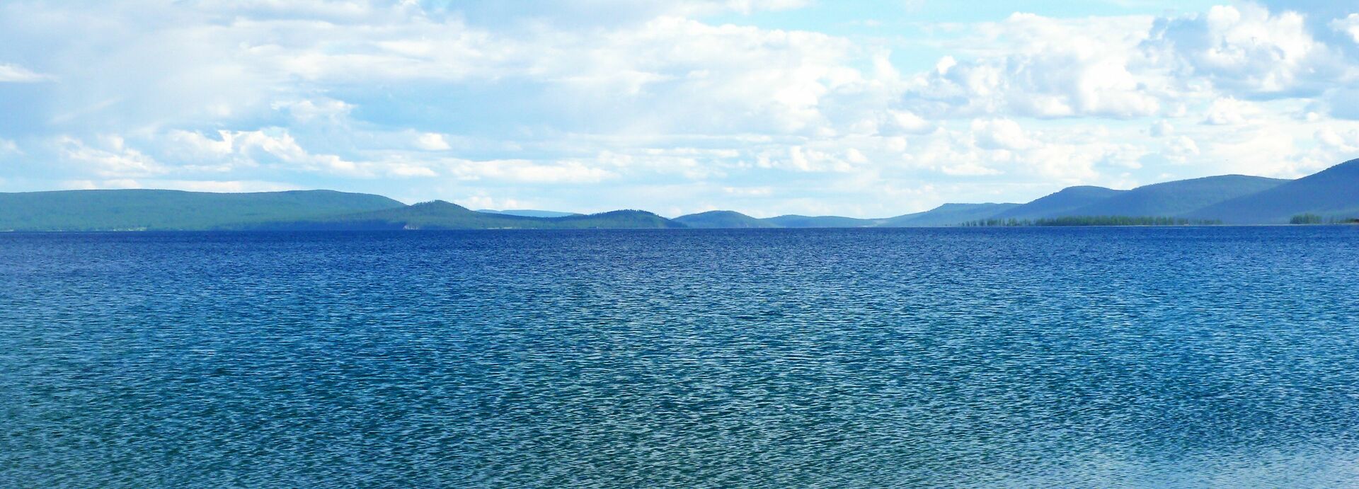 Eine blaue, gekräuselte Wasserfläche vor hügeligem Hintergrund