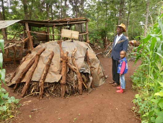 Ein älterer Mann und ein junges Mädchen begutachten einen mit Holz und Plane abgedeckten Reisighaufen.