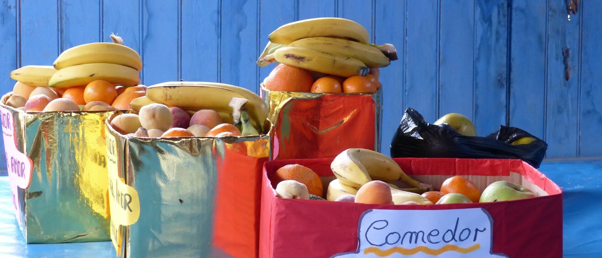 Golden und rot beklebte Kartons gefüllt mit Obst vor blauem Hintergrund