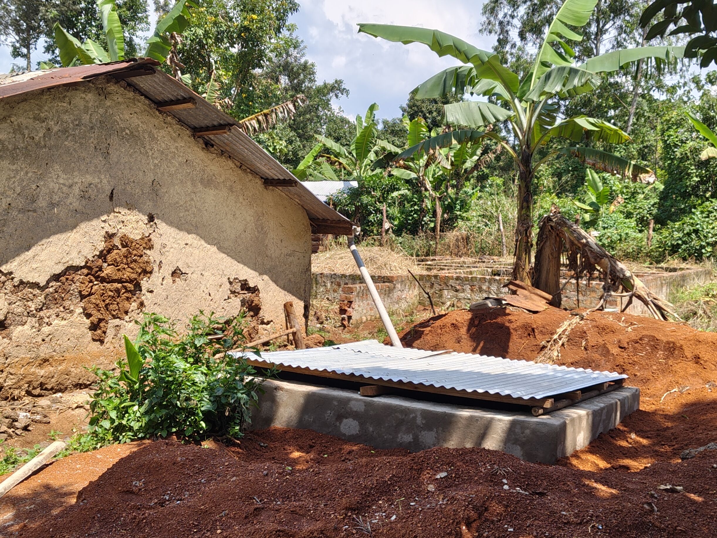 Links steht ein steinernes Gebäude mit Blechdach. Daneben steht ein viereckiges abgedecktes Becken, das mit einem Rohr mit dem Dach des Gebäudes verbunden ist.