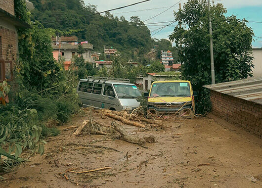 Ein verschlammter Straßenzug in Nepal. Schlammwasser drückt zwei Kleinbusse die Straße runter.